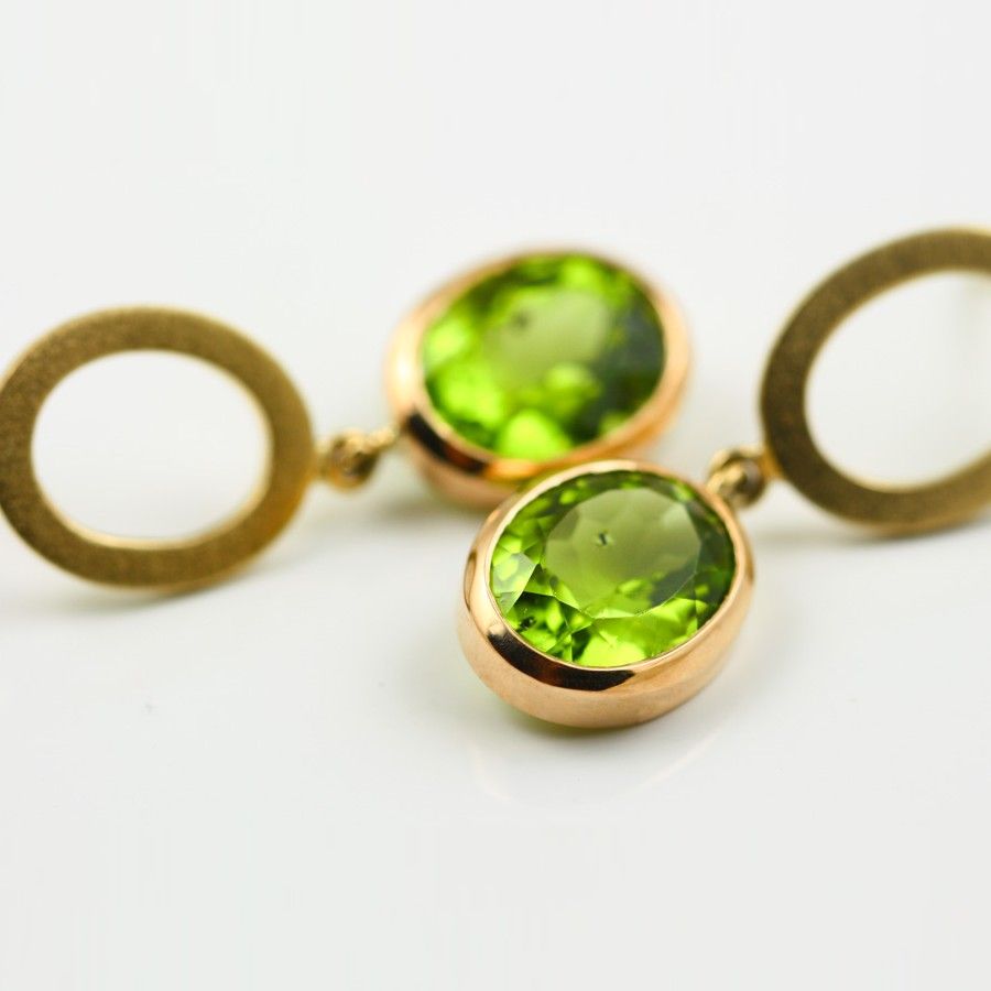 A pair of gold earrings, each a brushed open disc with a round peridot hanging below it